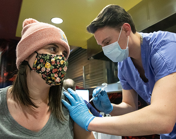 male healthcare worker giving vaccine to female in knit cap