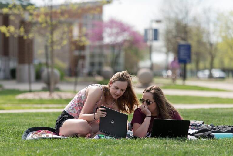 Two female students on blanked on the UIS quad looking at laptops