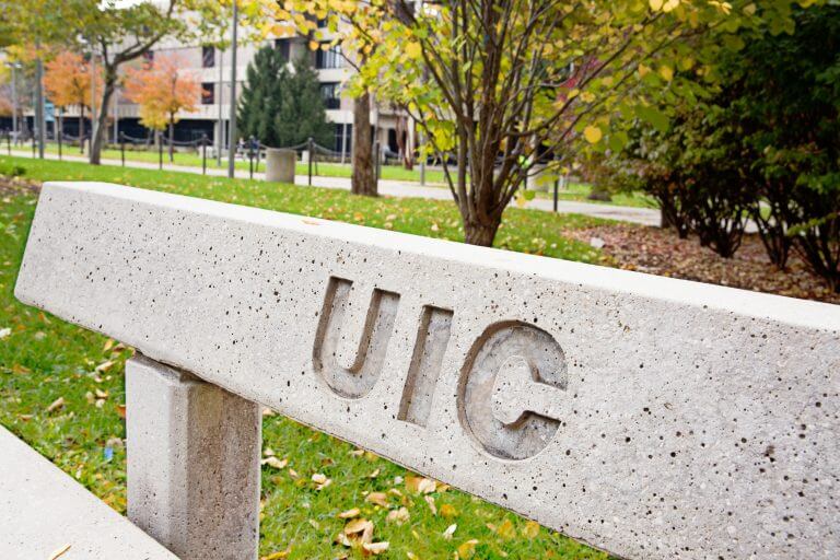 2016_11_11_fotolog-24-2-768x512.jpg Cement park bench with UIC engraved, in front of grassy/tree area on campus