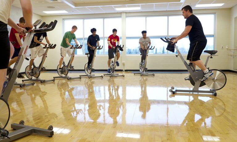23426408995_c0d7a259ee_o-768x461.jpg spinning class being led by male instructor in sunny gym
