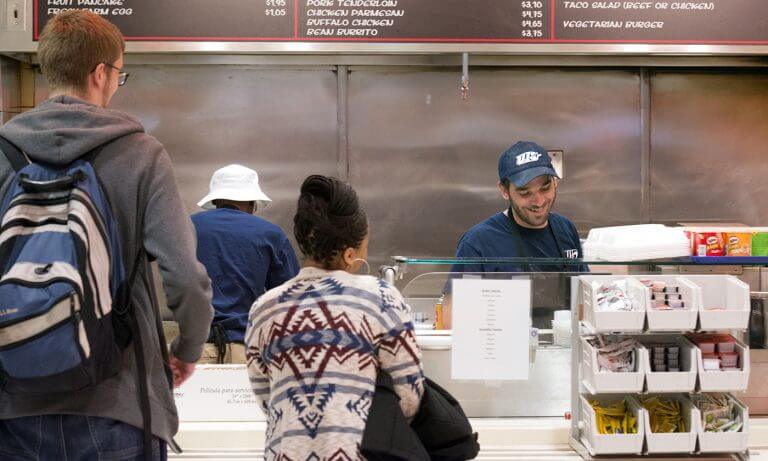 30945716351_c0462367f1_o-768x461.jpg students in line to get food from smiling worker in uniform at dining hall