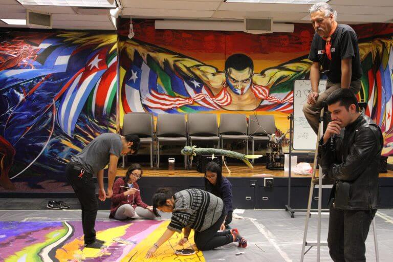 IMG_9726-2-768x512.jpg several students work on colorful mural on ground in office space with colorful diverse mural on wall